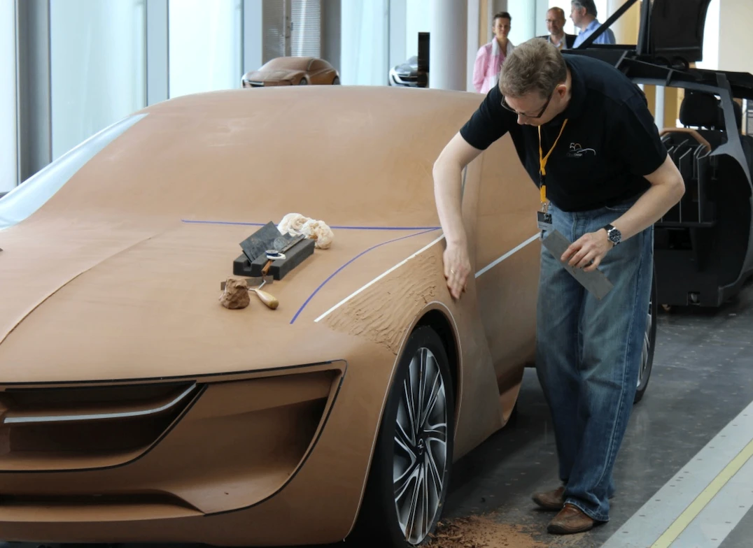 A designer shaping a full-size clay model of a car body